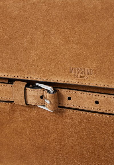 Geantă de umăr din suede maro cu închidere cu cataramă argintie. Are logo-ul embosat "Moschino Milano" și detalii cusute pe margini.