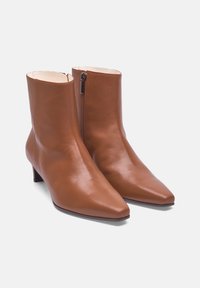 Bottines en cuir marron avec un bout pointu, un petit talon et une fermeture éclair sur le côté. Texture lisse avec un design épuré et minimaliste.