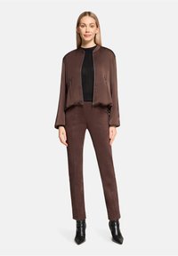 Brown satin bomber jacket with a zip front, paired with form-fitting brown suede trousers and black pointed ankle boots. Textured black top beneath.