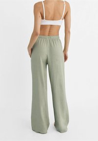 Pantalons vert clair, à coupe ample, fabriqués en tissu doux avec une taille élastique et un design à jambe droite. Texture lisse et détails minimaux.
