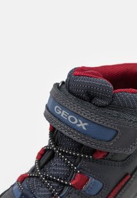 Wysokie sneakersy z granatową cholewką, czerwonymi akcentami i szarymi sznurówkami. Posiadają siateczkowy kołnierz, wyściełany język oraz gumową podeszwę. Widoczny logotyp marki.
