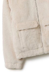 Chaqueta de pelo sintético en suave beige. Cuenta con dos bolsillos delanteros de parche, cierre con cremallera y un acabado texturizado y esponjoso. Diseño acogedor y cálido.
