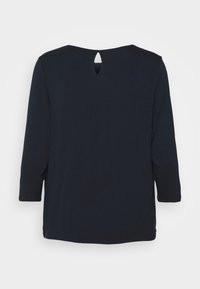 Mørkeblå langærmet top med rund halsudskæring og en nøglehuldetalje bagpå. Glat stof med sideslids i kanten for bedre bevægelsesfrihed.