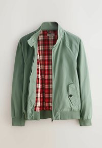 Veste en nylon verte avec col montant, poignets côtelés, poche extérieure et doublure intérieure en tartan rouge. Fermeture éclair visible.