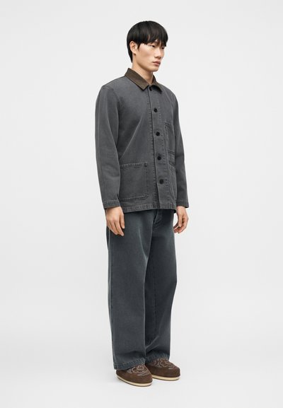 Σκούρο γκρι τζιν μπουφάν με καφέ γιακά, με κουμπιά και τσέπες. Συνδυασμένο με άνετο, χαλαρό σκούρο γκρι τζιν και καφέ παντόφλες.