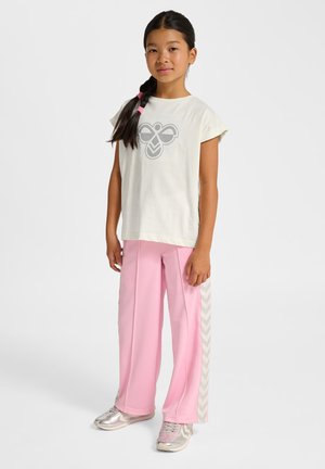 Lysebeige t-shirt med gråt grafisk design; lyserøde træningsbukser med tekstureret finish og sidestriber i fiskebenmønster. Sølvsko.