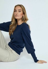 Maglione lavorato a maglia blu navy con maniche a palloncino e polsini a coste. Tessuto morbido, scollo rotondo, abbinato a pantaloni chiari.