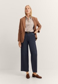 Brauner Blazer über einem gestreiften Button-down-Hemd, marineblaue weite Hose und braune Loafers. Einfaches, elegantes Design mit maßgeschneiderter Passform.