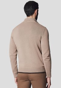 Beżowy sweter dziany z wysokim kołnierzem, prążkowanymi mankietami i długimi rękawami. Charakteryzuje się strukturalnym wykończeniem i bezszwowym wykończeniem ramion.