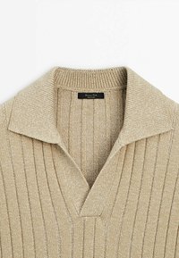 Pull en maille côtelée beige avec un large col retroussé et une ouverture en V, montrant l'étiquette de la marque à l'intérieur du col.