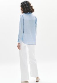 Camicia azzurra a maniche lunghe con dettaglio a bottone al polsino, abbinata a pantaloni bianchi a gamba larga. Tessuto morbido, vestibilità rilassata.