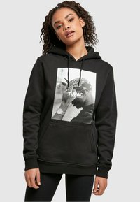 Sudadera negra con un gráfico de una figura que lleva un pañuelo. Bolsillo delantero y cordones en la capucha. Material textil suave.