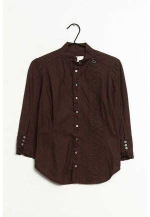 Blouse marron foncé à manches longues avec boutons sur le devant, col montant, détails cousus d'un côté et poignets boutonnés sur un cintre noir.