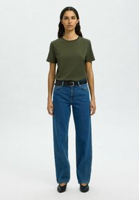 Olijfgroene katoenen t-shirt, blauwe wijde jeans met riem en zwarte puntige schoenen. Eenvoudig ontwerp met korte mouwen en een relaxed fit.