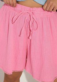 Rosa bomullsshorts med strukturerad yta, som har elastisk midja, rosett och dekorativ scalloped kant längs fållen.