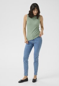 Grøn tekstureret ærmeløs top parret med lyseblå slim-fit jeans og sorte flade sko. Toppen har et ribbet mønster med en let ujævn kant.
