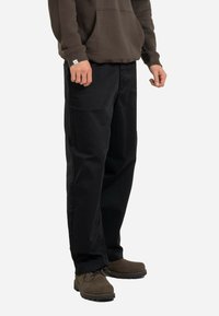 Black cotton pants with a straight cut, featuring two side pockets and a relaxed fit, worn with brown suede boots and a dark hoodie.