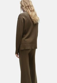 Rjav, teksturiran pleten pulover z sproščenim krojem, v kombinaciji s širokimi hlačami v istem odtenku, ki imata minimalne šive in čiste linije.