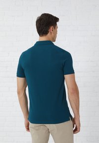 Tyrkisk polo skjorte med korte ermer og klassisk krave, laget av glatt stoff, med sideventiler og et rent, minimalistisk design.