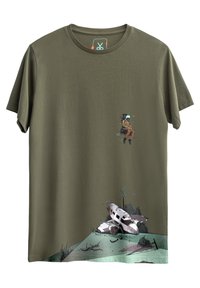 Olijfgroen katoenen t-shirt met een afbeelding van een zittende figuur in een oranje pak en een neergestort vliegtuig, verfraaid met bladeren.