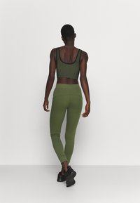 Oliven grøn træningsoutfit bestående af en ribbet crop top med sort kant og matchende højtaljede leggings, parret med sorte sneakers.