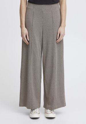 Weite Hose in einem braun-schwarzen karrierten Muster, mit Falten und einer glatten Stofftextur, kombiniert mit weißen Sneakers.