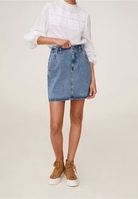 Jupe en jean avec un ourlet effiloché, dotée de deux poches avant et d'une silhouette ajustée. Associée à des baskets montantes marron clair.