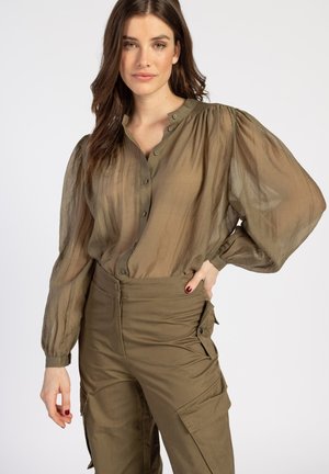 Olivgrüne, transparente Bluse mit langen, gepufften Ärmeln, Knopfleiste und lockerer Passform, kombiniert mit passenden Cargo-Hosen.