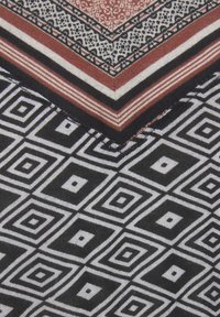 Musterstoff mit geometrischem Design, das schwarze und weiße Rauten sowie rote Akzente enthält, abgeschlossen mit einem kontrastierenden Rand.