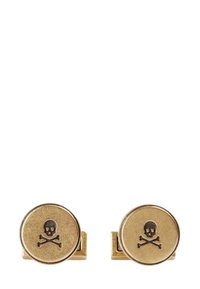 Gemelos de tono dorado con forma circular que presentan un diseño de calavera y huesos cruzados en color negro grabado en la superficie frontal.