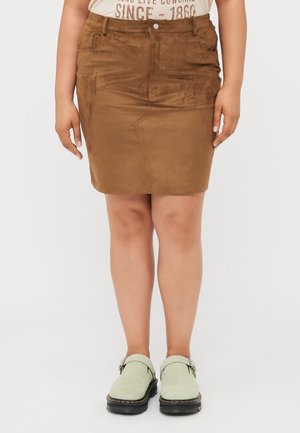 Brun semsket miniskjørt med en tettsittende design, frontlommer og knappelukking øverst, kombinert med lysegrønne slip-on sko.