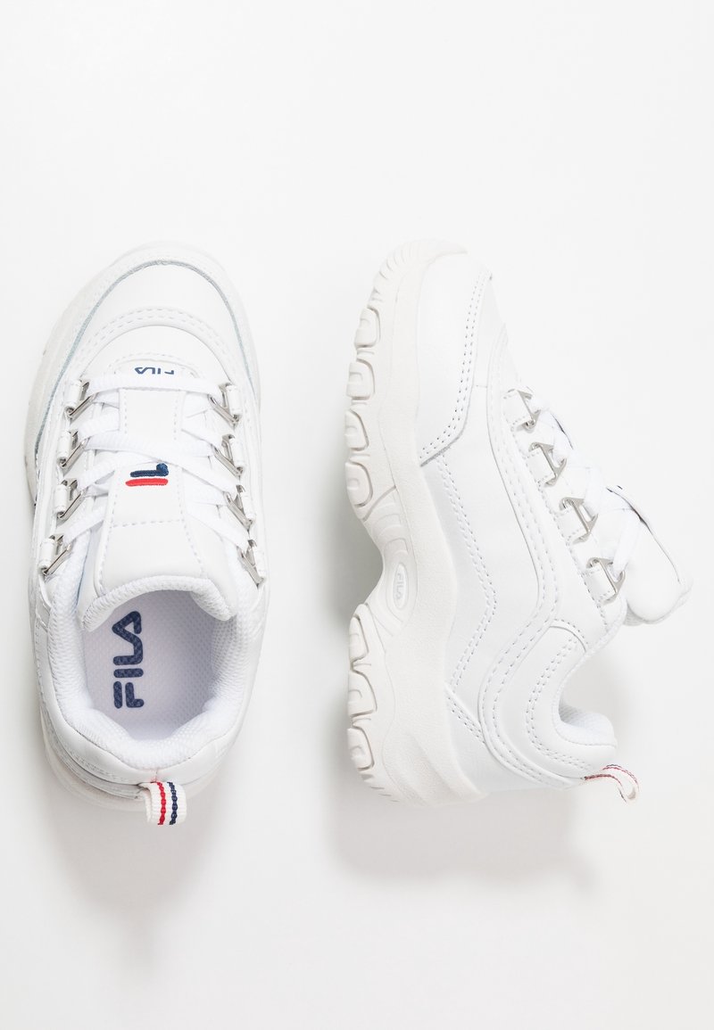 Paire de baskets blanches FILA avec semelles épaisses, œillets métalliques et détails du logo rouge, blanc et bleu sur fond blanc.