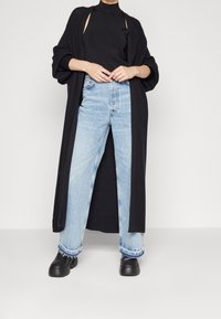 Cardigan nero lungo sopra un top nero senza maniche e jeans azzurri chiari a vita alta. Scarpe nere chunky con una texture liscia e orli sfrangiati.