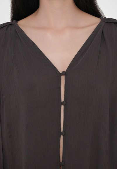 Dunkelgraue Bluse aus leichtem Stoff, mit V-Ausschnitt, Knopfverschlüssen und strukturierter Oberfläche mit subtilen Faltendetails.