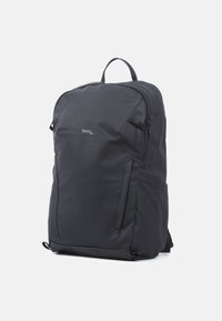 Sac à dos en nylon noir au design épuré et minimaliste. Il est équipé d'une poignée supérieure, de bretelles réglables et d'une poche frontale zippée.