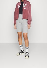 Röd satin zip-up jacka, svart topp, grå cykelshorts, svarta och vita randiga strumpor, svarta och vita sneakers med Adidas-loggor.