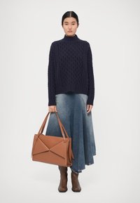 Navy cable-knit turtleneck sweater, light denim skirt with asymmetrical hem, brown leather handbag with geometric design, brown ankle boots.