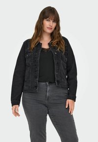 Svart denimjacka med klassisk design, med knappstängning, framfickor och en avslappnad passform. Bärs över en svart topp och gråbyxor.