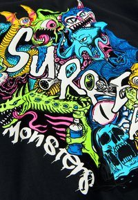 Black fabric featuring colorful graphic design with various monsters, skulls, and text. Prominent colors include green, blue, pink, and white.