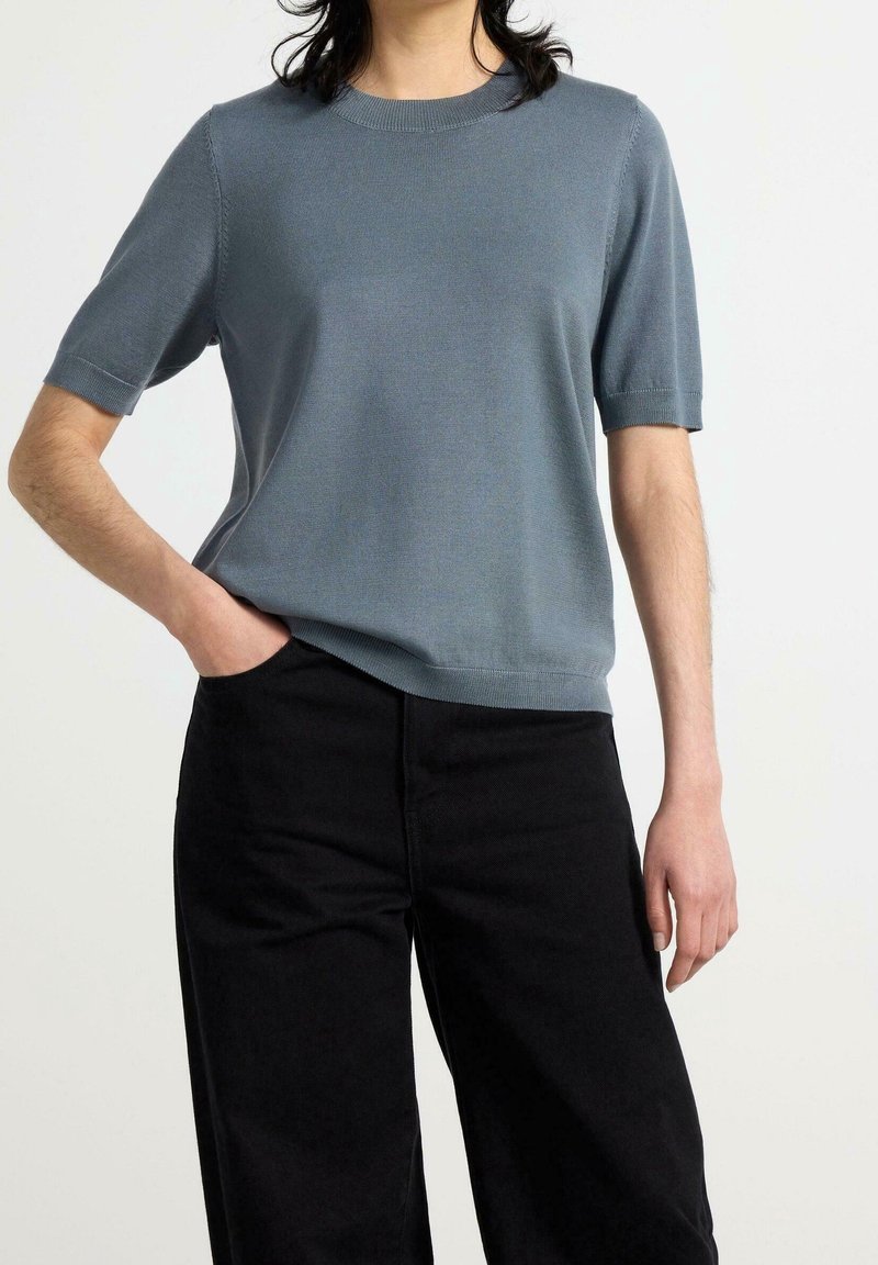 Suéter de punto de manga corta color azul claro con cuello redondo; textura suave y diseño ajustado; combinado con pantalones negros de cintura alta.