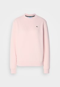 Ljusrosa sweatshirt gjord av texturerad bomull, med rund halsringning, ribbade ärmslut och en liten grön logotyp på vänster bröst.