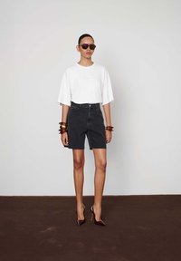 Valge ülepaisutatud T-särk, mustad teksashortsid ja pruuni värvi käevõrud. Pruuni värvi kontsadega kingad terava ninaga. Lihtne taust.