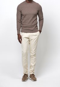 Brauner Strickpullover mit rundem Halsausschnitt, kombiniert mit beigen, schmal zulaufenden Hosen und braunen Wildledersneakern mit weißen Sohlen.