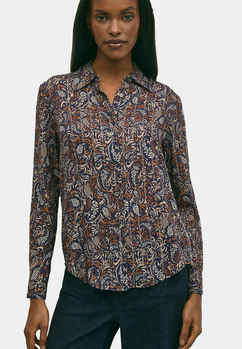 Camicia a maniche lunghe di colore navy con intricati motivi floreali in beige e ruggine. Presenta un colletto e una chiusura con bottoni. Tessuto liscio.