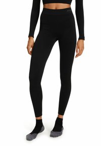 Schwarze Leggings aus elastischem Stoff mit hohem Bund. Glatte Textur und figurbetontes Design, kombiniert mit dunklen Socken.