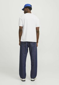 Hvid bomulds t-shirt og mørkeblå denim jeans med løs pasform, parret med en blå kasket. Enkel design uden synlige mønstre.