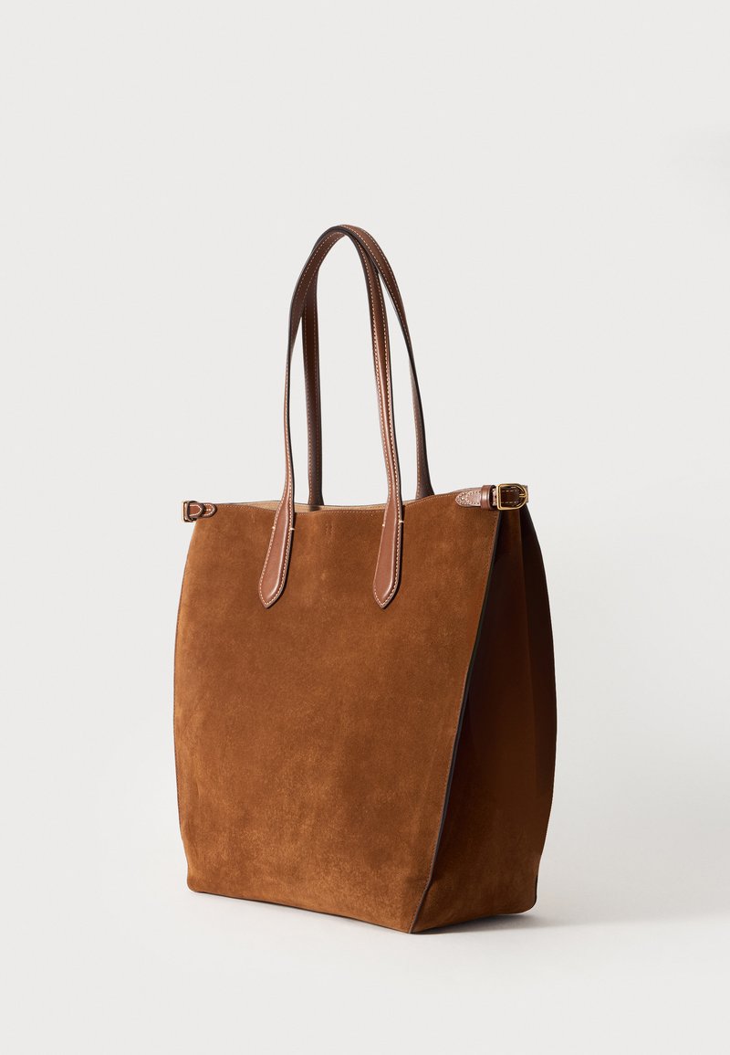 Sac cabas en daim marron avec double poignées longues en cuir lisse et détail de boucle latérale sur fond blanc.