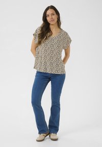 Haut à motifs léopard avec des manches courtes, décolleté en V, fond beige. Associé à un jean flare bleu et des baskets beiges. Design décontracté.