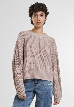 Pull en tricot rose clair avec un design court, un col rond côtelé et des manches amples, porté avec un jean en denim bleu.