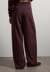 Weite Hosen aus dunkelburgunderfarbener Stoff. Glatte Textur, taillierte Verarbeitung mit Gesäßtaschen. Die Hose hat eine hohe Taille und einen fließenden Schnitt.